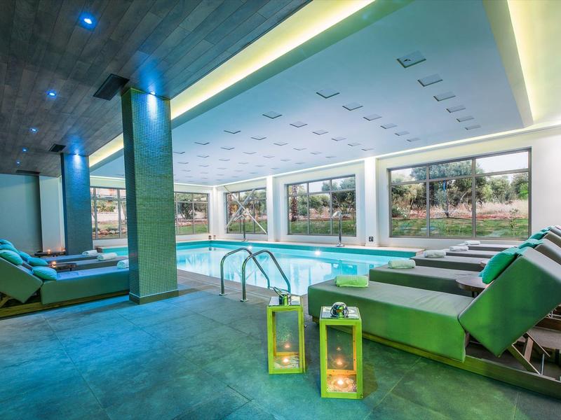 Moderner Innenpool mit Liegestühlen, großen Fenstern und stimmungsvoller Beleuchtung.