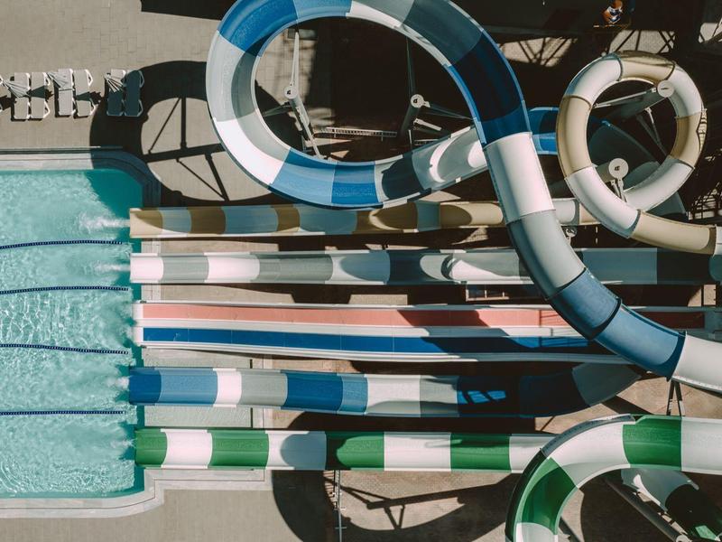 Vogelperspektive auf Schwimmbad mit Rutschen und Bahnen, klare Wasserfläche, Sonnenschein.