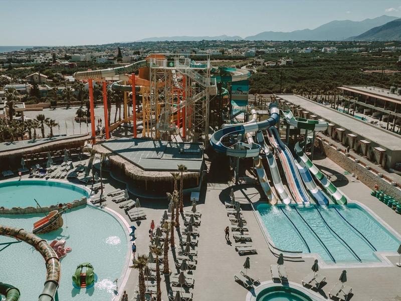 Freizeitpark mit Wasserrutschen, Schwimmbecken, Kletterwand und vielen Besuchern an einem sonnigen Tag.