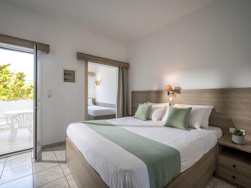 Helles Schlafzimmer mit großem Bett, Holzmöbeln und Zugang zu Balkon mit weißem Stuhl.