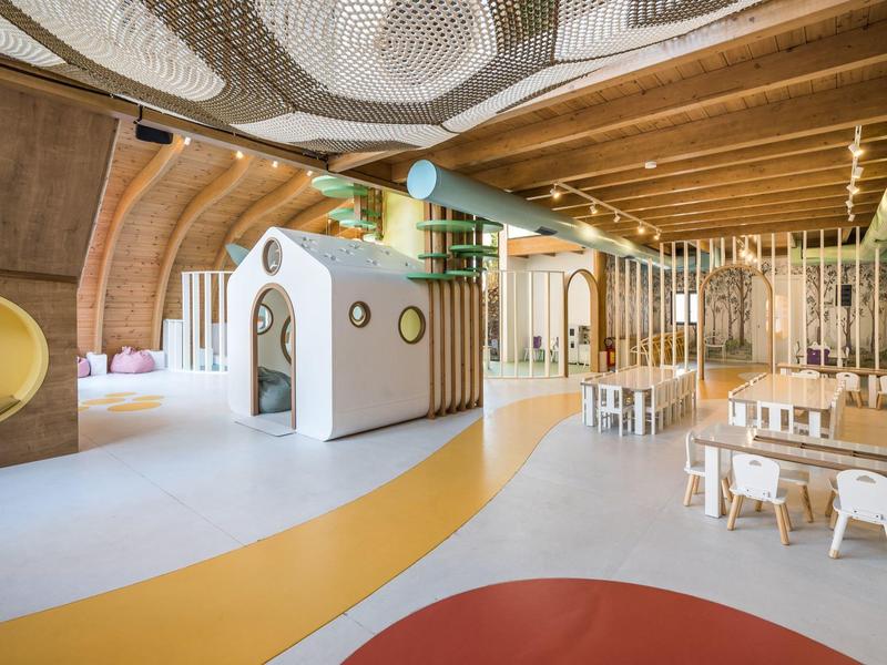 Heller, moderner Kindergarten mit Holzdecken, buntem Boden und kindgerechten Möbeln.