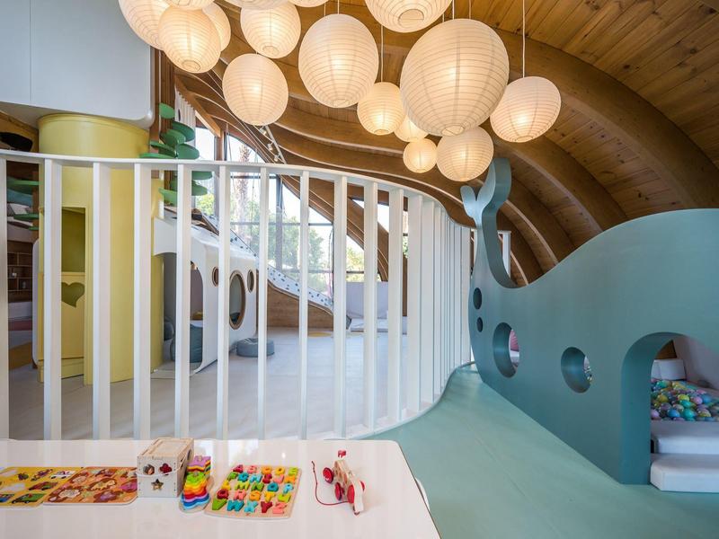 Hell eingerichteter, moderner Kinderbereich mit buntem Holzspielzeug und großen Kugel-lampen.