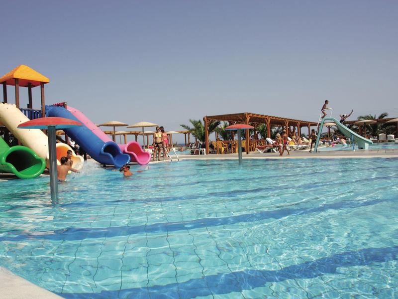Großer Pool mit Wasserrutschen, sonnigem Himmel und Liegestühlen im Hintergrund.