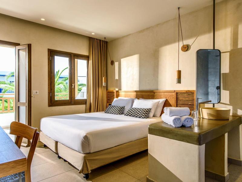 Helles Hotelzimmer mit Doppelbett, Holzmöbeln, Fenstern zu Balkon und modernen Badaccessoires.