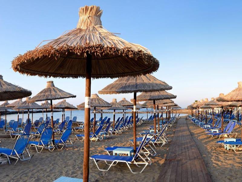 Strand mit vielen blauen Liegestühlen und Strohschirmen unter klarem, blauem Himmel.