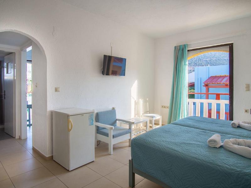 Světý hotelový pokoj s postelí, televizí, lednicí a balkonem s výhledem.