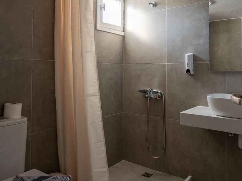 Malá koupelna se sprchovým koutem, bílou toaletou a umyvadlem, šedé dlaždice.