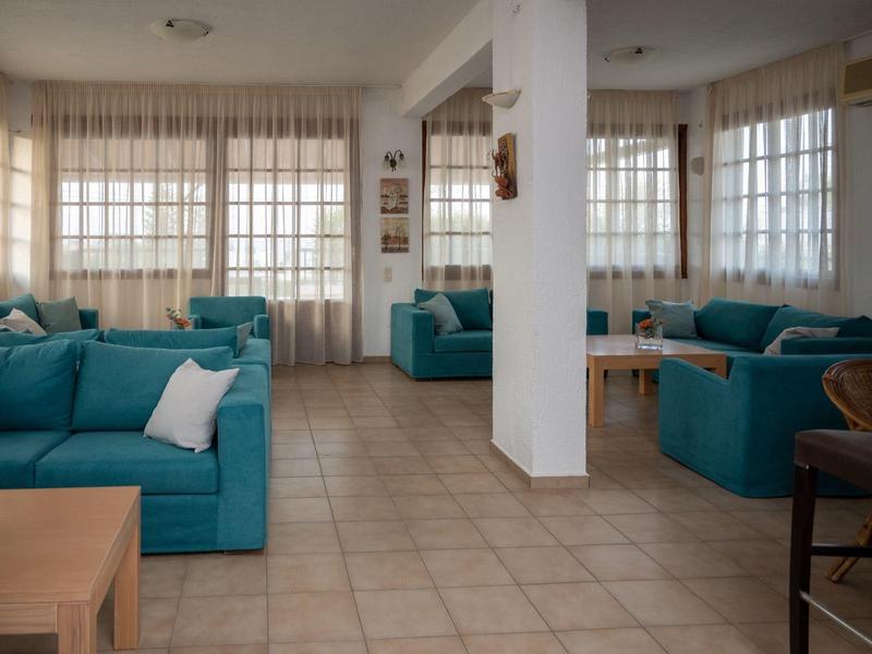 Jasný obývací pokoj s modrými pohovkami, polštáři a velkými okny s záclonami.