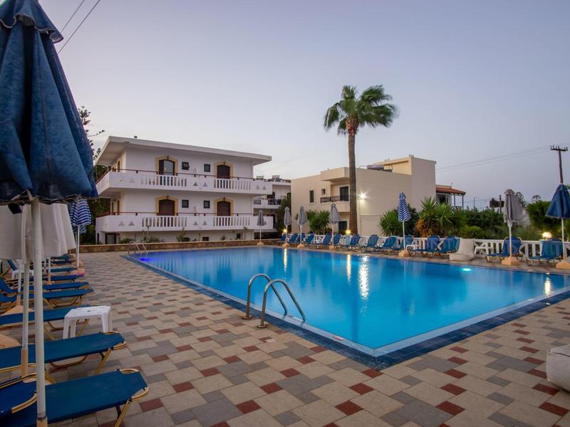 Jasné osvětlení bazénu při západu slunce před hotelem s lehátky a slunečníky.