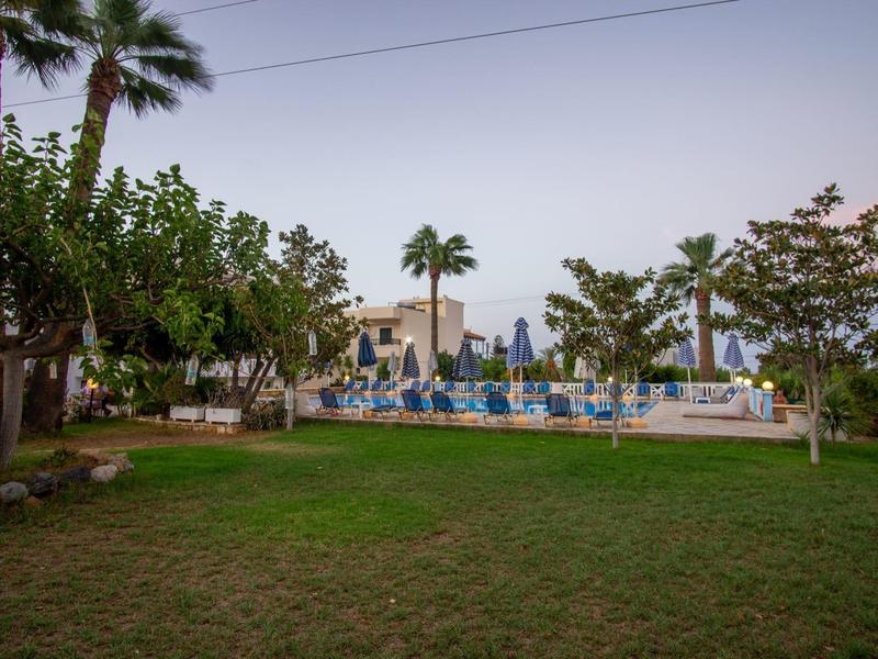 Zelená zahrada s bazénem a modrými lehátky v hotelovém komplexu při západu slunce.