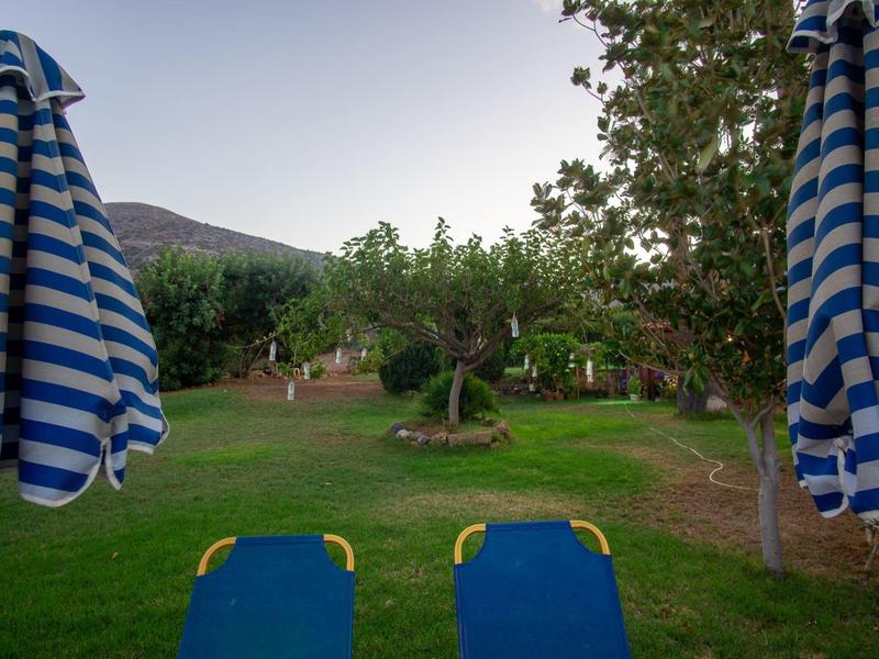 Dva modré lehátka s modro-bílými pruhovanými slunečníky na zahradě s stromy a horami v pozadí.