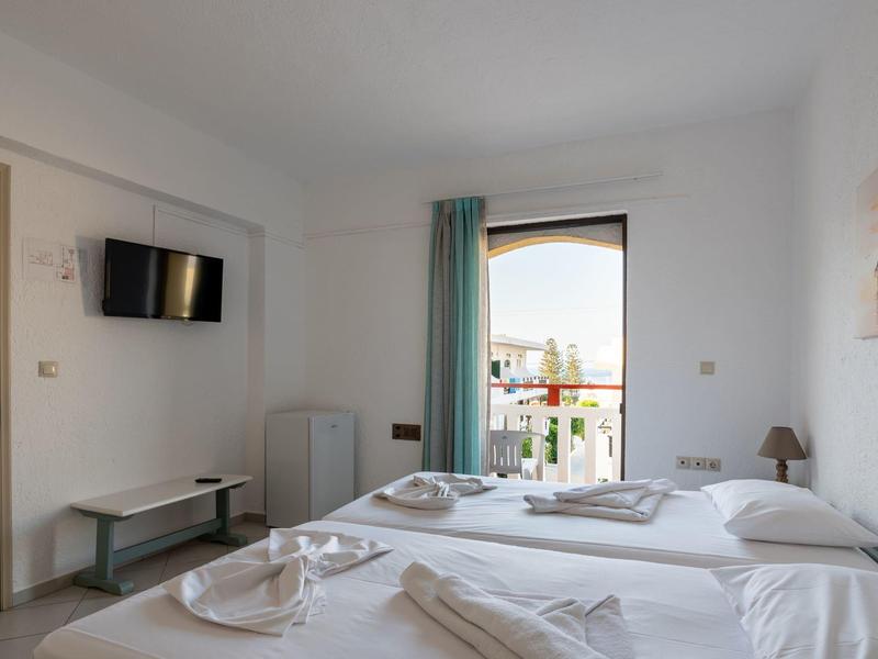 Moderně zařízený hotelový pokoj se dvěma jednolůžky, balkonem a televizí na zdi.