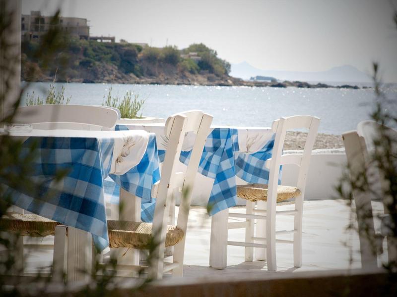 Tavolo vuoto con tovaglia a quadri blu e bianca su una terrazza con vista mare.