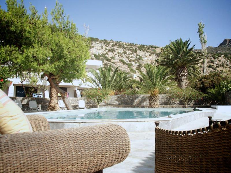 Area piscina con mobili in vimini, alberi e colline sullo sfondo con tempo soleggiato.