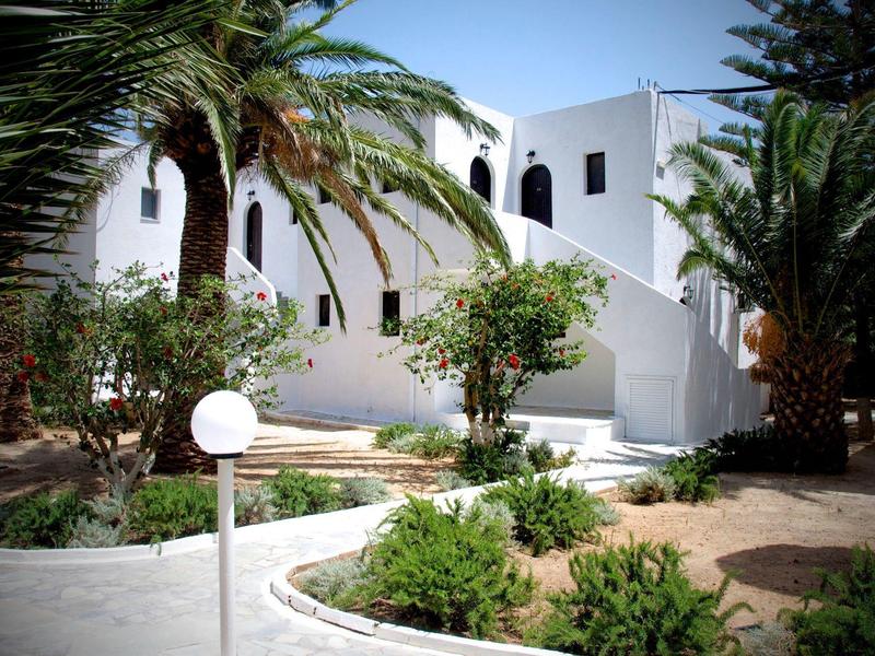 Edifici bianchi circondati da palme verdi e sentieri sotto un cielo blu.