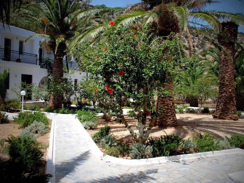 Cortile con palme e giardino curato davanti a un edificio bianco in posizione soleggiata.