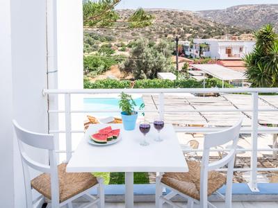 Stůl na balkoně se dvěma sklenicemi vína, vodou a občerstvením s výhledem na slunečnou krajinu.