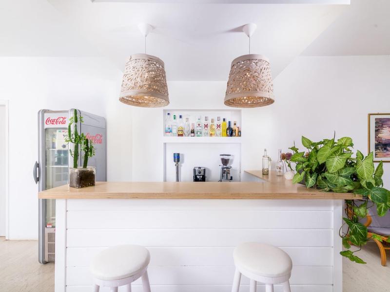 Moderne hotelbar met witte krukken, houten toonbank en planten in een lichte omgeving.