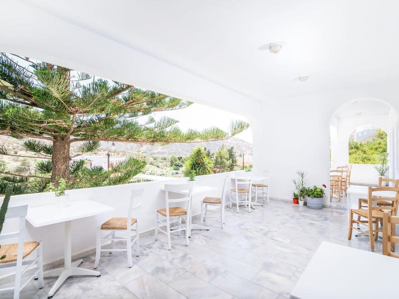 Heldere terras met witte tafels en stoelen, omgeven door groen gebladerte en uitzicht op heuvels.