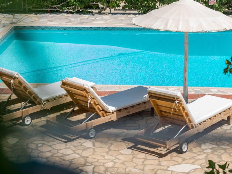 Drie ligstoelen met witte kussens naast een blauw zwembad en een parasol.
