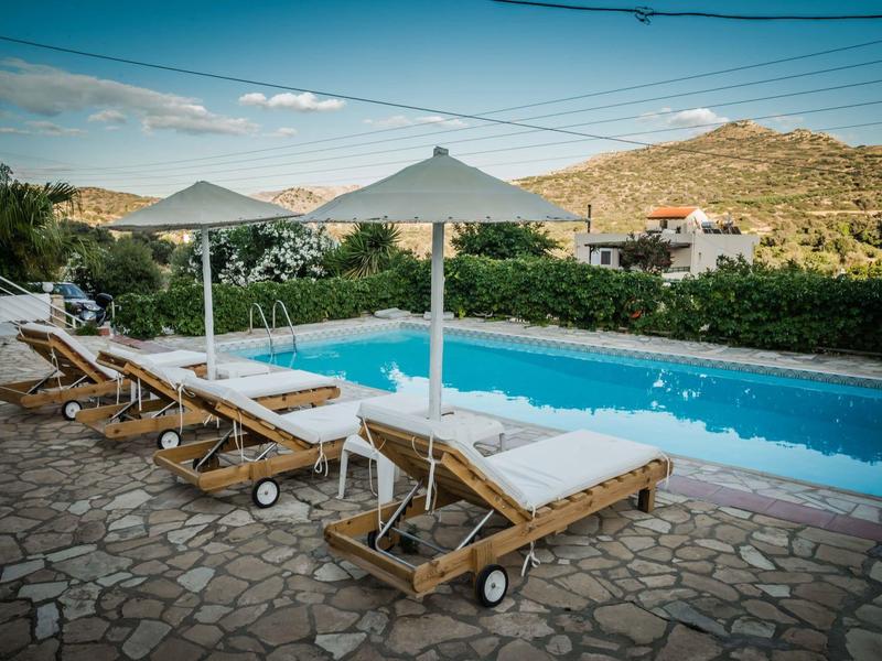 Vier ligstoelen met witte kussens en parasols bij het zwembad met heuvelachtig landschap.