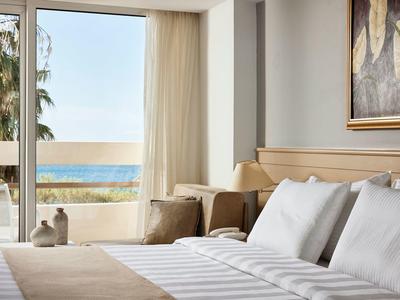 Jasny pokój hotelowy z łóżkiem podwójnym i widokiem na morze przez duże okno.