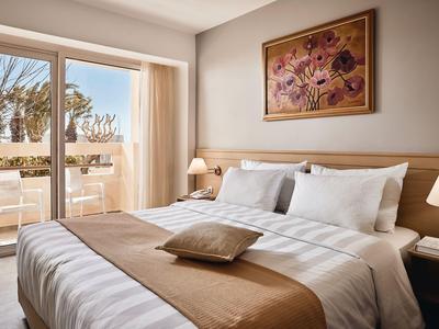 Cozy hotel room with double bed, lamps, and balcony with outdoor furniture.