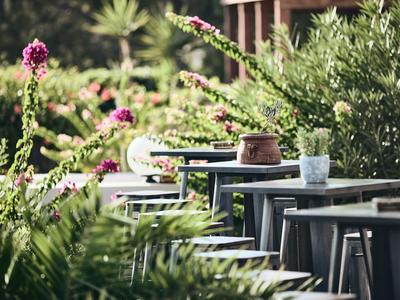 Taras na zewnątrz z krzesłami i stołami otoczony zielonymi roślinami i kwiatami.