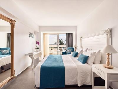 Nowoczesny pokój hotelowy z podwójnym łóżkiem, dużym lustrem i balkonem z widokiem na morze.