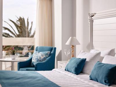 Nowoczesny pokój hotelowy z biało-niebieską dekoracją i balkonem z widokiem na palmy.