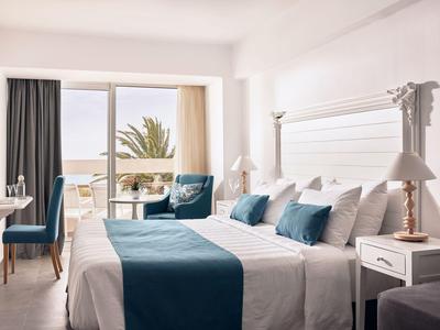 Bright hotel room with double bed, blue accents, and balcony with sea view.