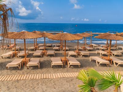 Row of beach loungers with straw umbrellas by the sea under a blue sky.