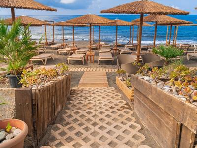 Restauracja na plaży z drewnianymi meblami, słomianymi dachami i widokiem na niebieskie morze.