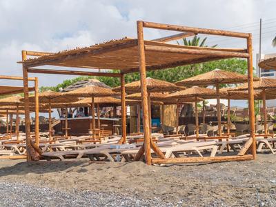 Puste leżaki pod drewnianymi pawilonami na kamienistej plaży pod pochmurnym niebem.