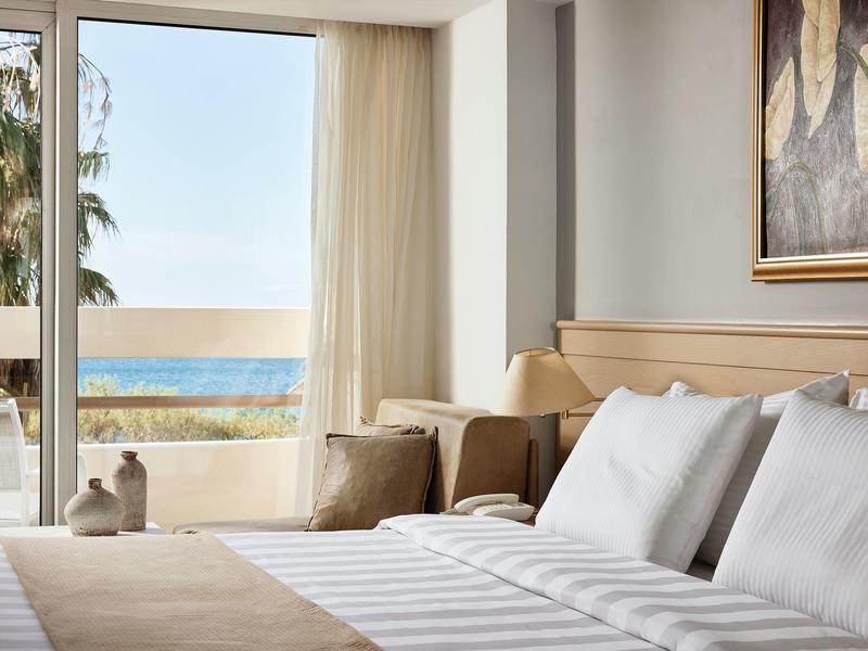 Jasny pokój hotelowy z łóżkiem podwójnym i widokiem na morze przez duże okno.