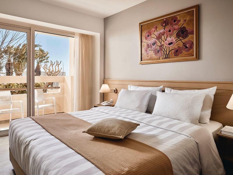 Przytulny pokój hotelowy z dużym łóżkiem, balkonem i kwiatową dekoracją na ścianie.