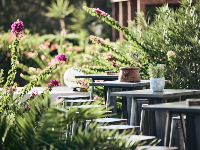 Taras na zewnątrz z krzesłami i stołami otoczony zielonymi roślinami i kwiatami.