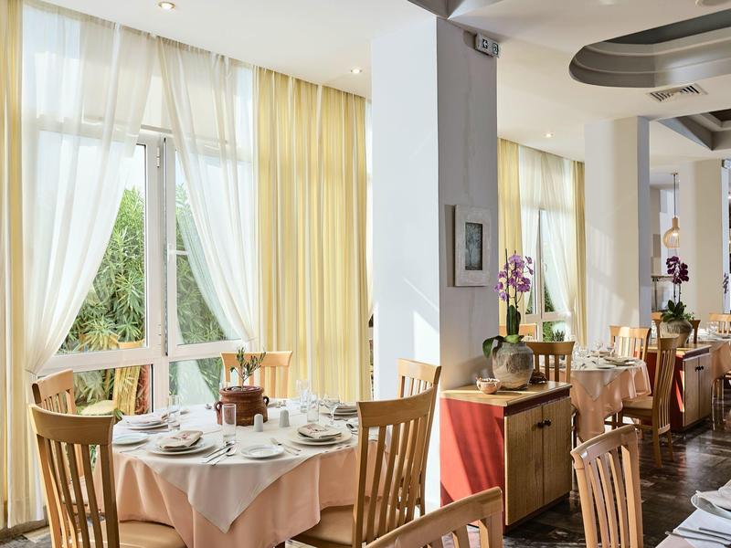 Przytulna sala śniadaniowa z nakrytymi stołami i dużymi oknami z żółtymi zasłonami.