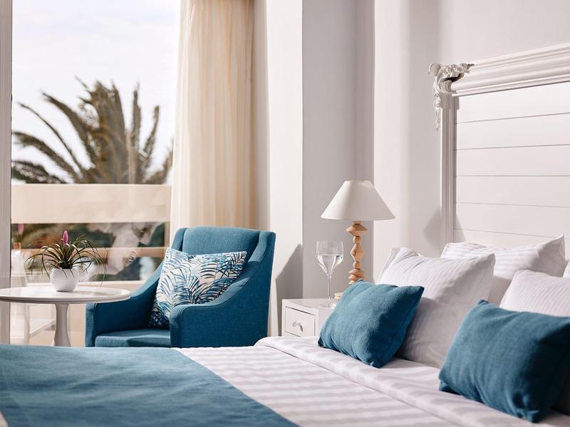 Nowoczesny pokój hotelowy z biało-niebieską dekoracją i balkonem z widokiem na palmy.