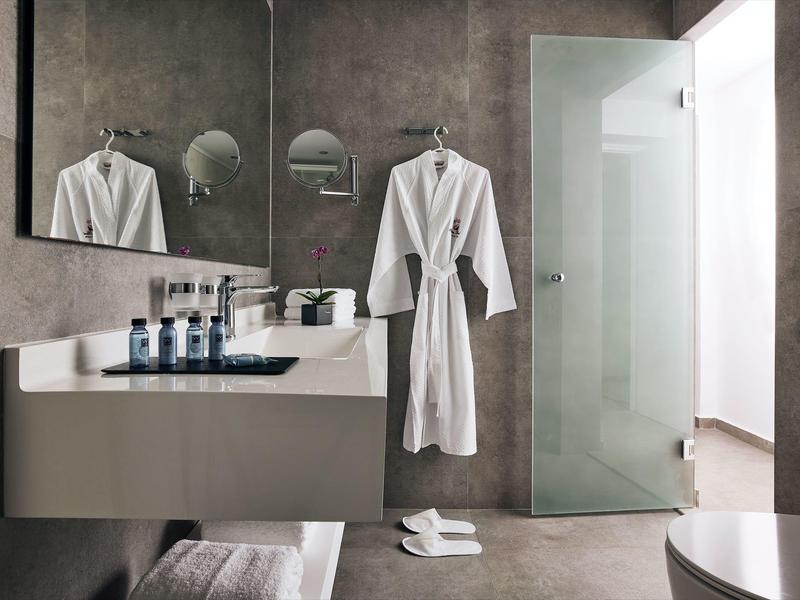 Nowoczesna łazienka z umywalką, ręcznikami, szlafrokiem i szklanymi drzwiami.