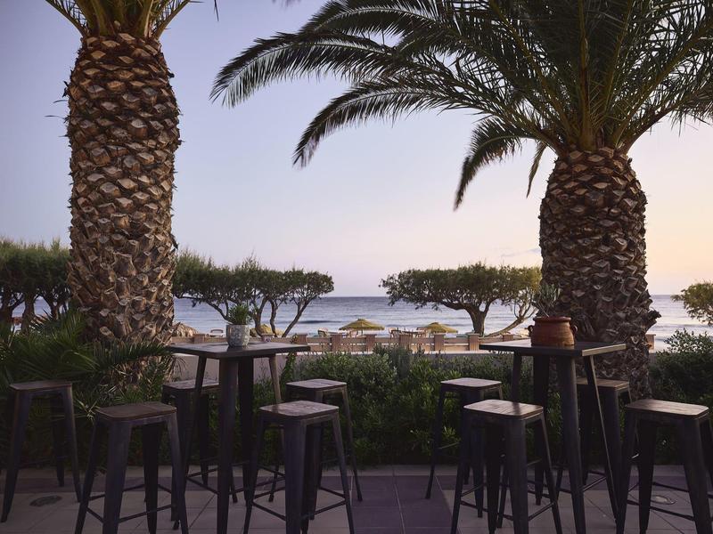 Taras z hokerami pod palmami z widokiem na morze o zachodzie słońca.