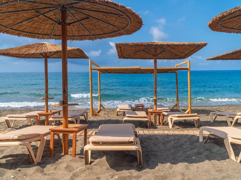 Plaża z leżakami i parasolami przy spokojnym morzu pod niebieskim niebem.