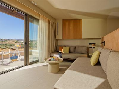 Modernes Hotelzimmer mit Sofa, Kaffeetisch und großer Glas-Schiebetür zum Balkon mit Meerblick.