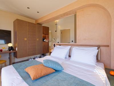 Helles Hotelzimmer mit Doppelbett, bunten Kissen und modernem Mobiliar.