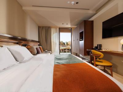 Modern eingerichtetes Hotelzimmer mit großem Bett, Schreibtisch und Balkonblick auf Stadt.