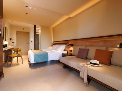 Modernes Hotelzimmer mit Doppelbett, Sofa, Holzmöbeln und warmem Licht.