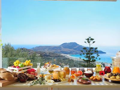 Table de petit-déjeuner avec divers aliments et boissons face à la mer et aux montagnes.