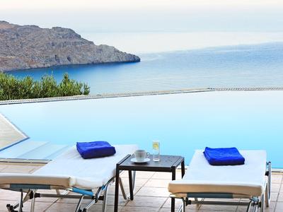 Piscine à débordement avec vue sur la mer et chaises longues avec serviettes bleues par une journée ensoleillée