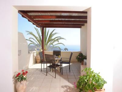 Terrazza coperta con sedie e tavolo con vista sul mare e palme.