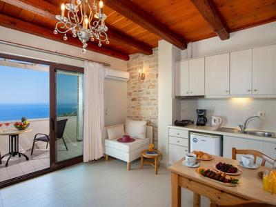 Soggiorno luminoso con soffitto a travi di legno, porta aperta su balcone con vista mare